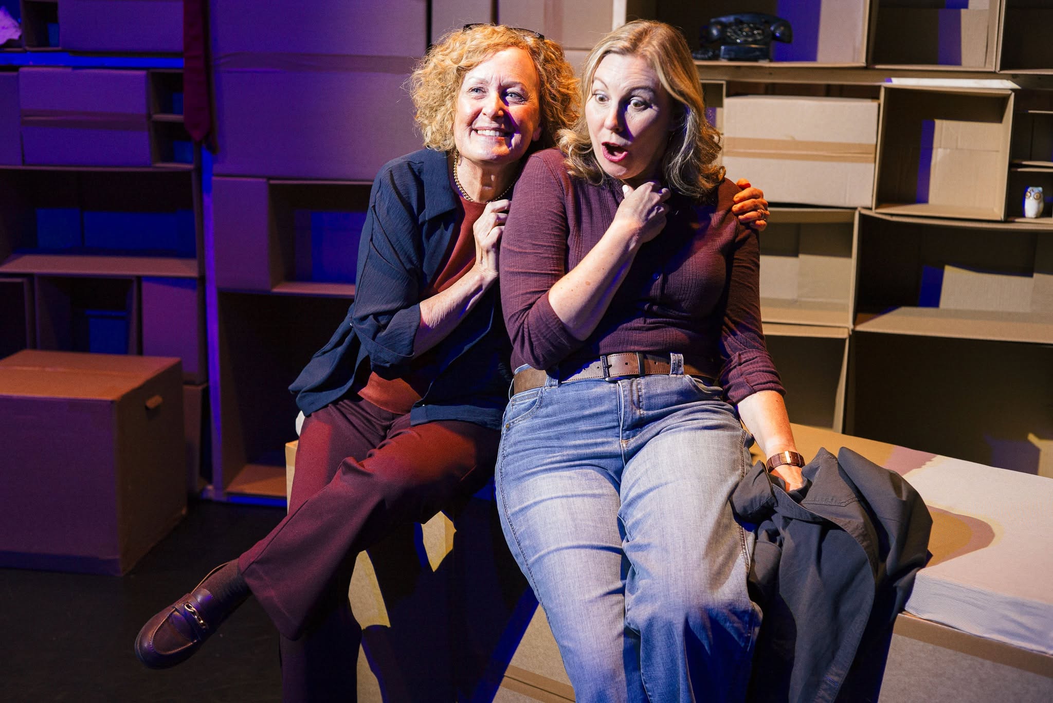 Two people share a close, intimate moment on a lit circular stage under a hanging paper lantern, surrounded by colorful stools in blue light.